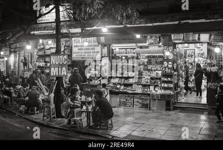 Vietnamesische Menschen sitzen abends in einem Straßencafé und trinken Zuckerrohrsaft im Zentrum von Hanoi, Vietnam. Stockfoto