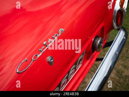 Der Name auf dem hinteren Kofferraum (Kofferraum) eines hellroten 1965 Mark 1 (MK1) Ford Cortina Deluxe wird bei einer Oldtimer-Veranstaltung in Storrington, West Sussex, Großbritannien, ausgestellt Stockfoto