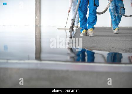 Erntegutarbeiter, die selbstnivellierenden Betonboden ausgießen Stockfoto