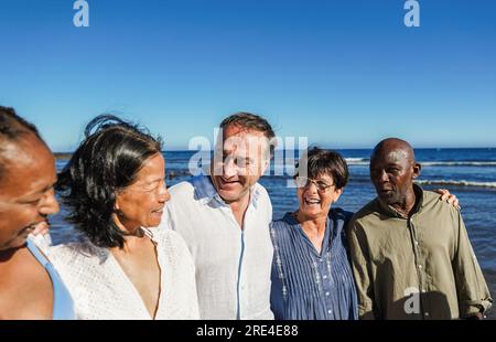 Glückliche Senioren, die bei Sonnenuntergang am Strand spazieren gehen und Sommerkleidung tragen - fröhlicher Lebensstil, Urlaub und Reisekonzept für ältere Menschen - Hauptfo Stockfoto