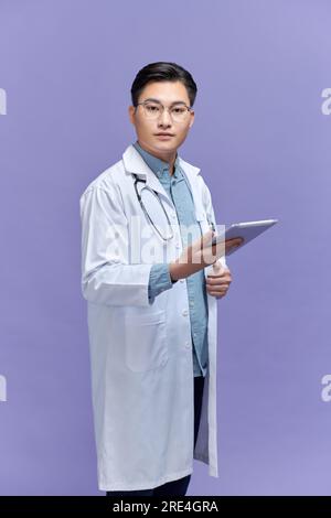 Ein freundlicher asiatischer Arzt in einem weißen Kittel und einem schwarzen Stethoskop mit einem Tablet-Computer, Stockfoto