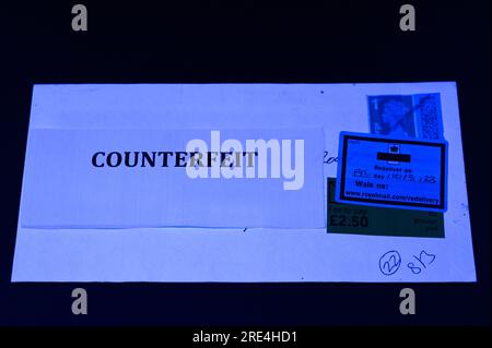 England, 25. Juli 2023: Wenn ein gefälschter Royal Mail-Stempel per Post entdeckt wird, wird er zurückgehalten, bis der Empfänger eine Gebühr bezahlt, da er als „kein Porto bezahlt“ vermerkt ist. - Gefälschte Royal Mail-Strichcodes werden auf eBay zu einem Bruchteil des Originalpreises verkauft. Bögen mit 50 Briefmarken werden ab 15 Pfund (GBP) verkauft und sehen für den ahnungslosen Blick echt aus. Unter UV-Licht sind jedoch kleine Unterschiede zu erkennen. Kredit: Stop Press Media/Alamy Live News Stockfoto