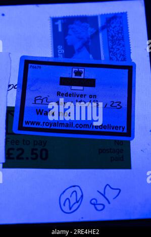 England, 25. Juli 2023: Wenn ein gefälschter Royal Mail-Stempel per Post entdeckt wird, wird er zurückgehalten, bis der Empfänger eine Gebühr bezahlt, da er als „kein Porto bezahlt“ vermerkt ist. - Gefälschte Royal Mail-Strichcodes werden auf eBay zu einem Bruchteil des Originalpreises verkauft. Bögen mit 50 Briefmarken werden ab 15 Pfund (GBP) verkauft und sehen für den ahnungslosen Blick echt aus. Unter UV-Licht sind jedoch kleine Unterschiede zu erkennen. Kredit: Stop Press Media/Alamy Live News Stockfoto
