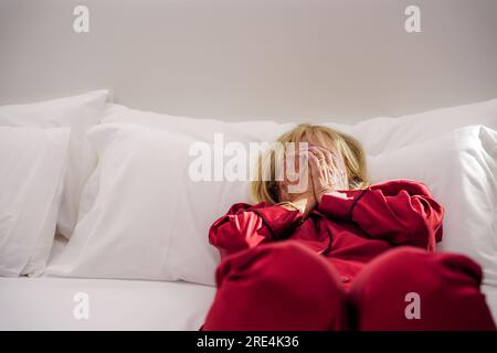 Eine Frau mittleren Alters, die auf dem Bett liegt, fühlt sich erschöpft, ängstlich und aufgebracht. Psychische Gesundheit Stockfoto