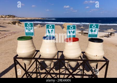 Vier Behälter für Mülltrennung und Recycling. Grüne, blaue, rote und schwarze Markierungen auf Müllbehältern für Papier, Kunststoff, Glas und Metall am Strand Stockfoto