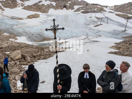 Garmisch Partenkirchen, Deutschland. 25. Juli 2023. Der katholische Priester Florian Hammerl (3. von rechts) und der protestantische Priester Uli Wilhelm (r) halten vor den Überresten des Gletschers (im Hintergrund), eine Prozession für den Zugspitz-Gletscher. Zusätzlich zu Informationen und Gebeten wird der Gletscher gesegnet und ein für den Anlass zusammengestelltes Bergquiem wird mit drei Sängerinnen und einem Windchor Premiere erhalten. Kredit: Peter Kneffel/dpa/Alamy Live News Stockfoto