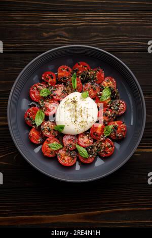 Burrata mit gebackenen Kirschtomaten und Gewürzen, auf einem Teller Stockfoto