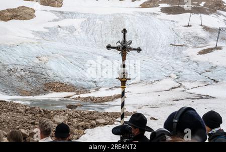 Garmisch Partenkirchen, Deutschland. 25. Juli 2023. Während einer Prozession steht ein Kreuz mit Schädel vor den Überresten des Gletschers (im Hintergrund) auf dem Zugspitz-Gletscher. Neben Informationen und Gebeten wird der Gletscher gesegnet und ein für den Anlass zusammengestelltes Bergquiem wird mit drei Sängerinnen und Windchor Premiere erhalten. Kredit: Peter Kneffel/dpa/Alamy Live News Stockfoto