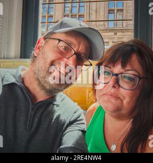 Ein Paar mittleren Alters mit Brille saß im öffentlichen Haus und lächelte vor der Kamera. Modellveröffentlichungen sind verfügbar, falls erforderlich. Stockfoto