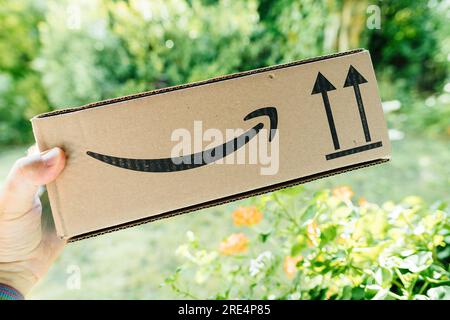 Hamburg, Deutschland - 24. Juli 2023: POV männliche Hand hält neues Amazon Prime Papppäckchen mit Gartengrün hinterlegt Stockfoto