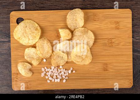 Kartoffelchips auf einem Holzbrett mit grobem Salz eignen sich gut für Bier oder Ale-Snacks auf einem Holztisch. Gut für Bierfestivals, Kneipen, Restaurantwerbung Stockfoto