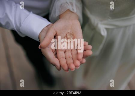 Die Hand des Bräutigams hält die Hand der Braut mit zwei goldenen Hochzeitsringen auf ihrer Handfläche. Nahaufnahme. Stockfoto