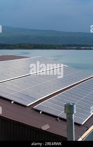 Nahaufnahme von Sonnenkollektoren auf dem Dach eines Hauses im Hintergrund eines Sees, Berge. Vertikales Foto Stockfoto