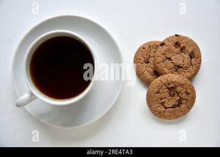 Teepaar und Haferflocken-Kekse mit Schokolade auf weißem Hintergrund. Köstliches Mittagessen mit Tee und süßen Plätzchen. Porzellantee-Set mit einem heißen Getränk. Gute Güte Stockfoto