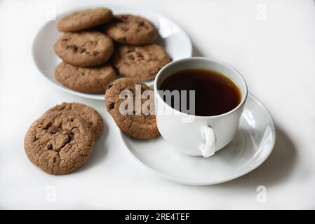 Teepaar und Haferflocken-Kekse mit Schokolade auf weißem Hintergrund. Köstliches Mittagessen mit Tee und süßen Plätzchen. Porzellantee-Set mit einem heißen Getränk. Gute Güte Stockfoto