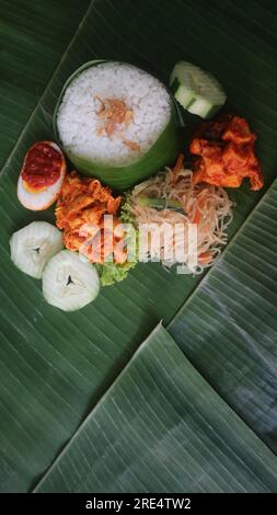 Schmackhafter Reis, Nudeln, Gurken und gewürzte Kartoffeln auf Bananenblatt. Traditionelles indonesisches Essen Stockfoto