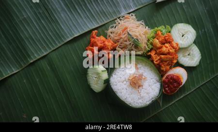 Schmackhafter Reis, Nudeln, Gurken und gewürzte Kartoffeln auf Bananenblatt. Traditionelles indonesisches Essen Stockfoto