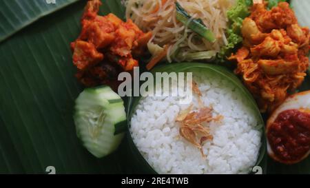 Schmackhafter Reis, Nudeln, Gurken und gewürzte Kartoffeln auf Bananenblatt. Traditionelles indonesisches Essen Stockfoto