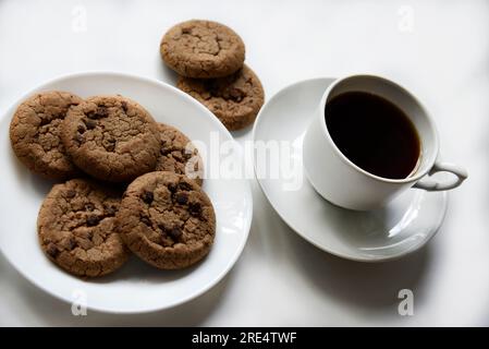 Teepaar und Haferflocken-Kekse mit Schokolade auf weißem Hintergrund. Köstliches Mittagessen mit Tee und süßen Plätzchen. Porzellantee-Set mit einem heißen Getränk. Gute Güte Stockfoto