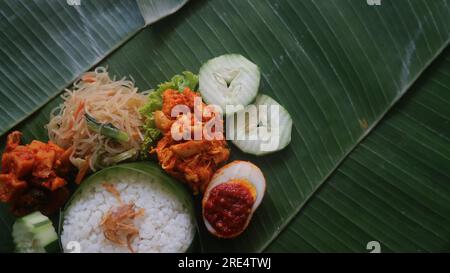 Schmackhafter Reis, Nudeln, Gurken und gewürzte Kartoffeln auf Bananenblatt. Traditionelles indonesisches Essen Stockfoto