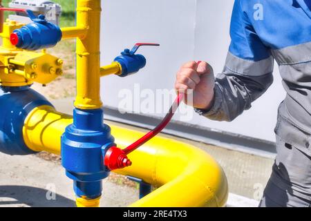 Der Techniker schließt den Hahn der Gasleitung. Abschaltung der Erdgasversorgung Die Hand des Mannes wird rot auf dem gelben Rohr. Hintergrund. Stockfoto