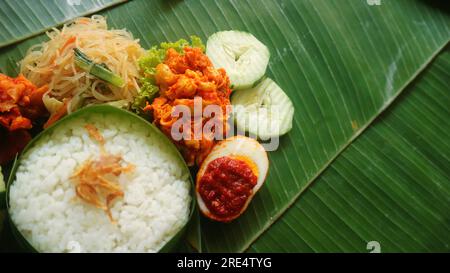 Schmackhafter Reis, Nudeln, Gurken und gewürzte Kartoffeln auf Bananenblatt. Traditionelles indonesisches Essen Stockfoto