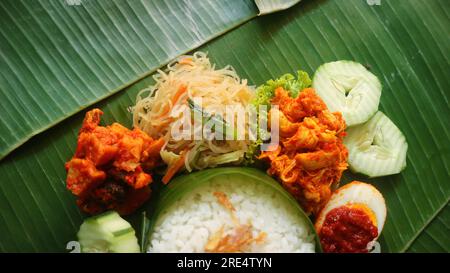 Schmackhafter Reis, Nudeln, Gurken und gewürzte Kartoffeln auf Bananenblatt. Traditionelles indonesisches Essen Stockfoto