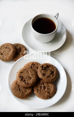 Teepaar und Haferflocken-Kekse mit Schokolade auf weißem Hintergrund. Köstliches Mittagessen mit Tee und süßen Plätzchen. Porzellantee-Set mit einem heißen Getränk. Gute Güte Stockfoto