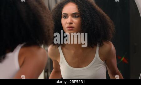 Besorgte junge, wunderschöne afroamerikanische Frau trauriges, ethnisches Mädchen, das in den Spiegel schaute, gestresst über Gesichtsfalten Problem Akne frustrierte, verärgerte Berührung Stockfoto