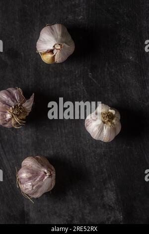 Frische Knoblauchknollen auf schwarzem Hintergrund. Flach verlegt. Draufsicht. Speisekonzept. Dunkle Stimmungsfotografie. Stockfoto