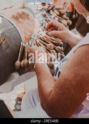 Hände einer Frau, die Spulenstickerei in einer Werkstatt weben. Lacemaker-Frau bei der Arbeit, traditionelles Schnürsenkel-Kunsthandwerk, Volkskunst, selektive Fokussierung Stockfoto