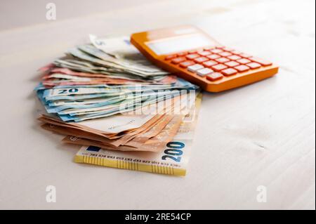 Ein Haufen verschiedener Euro-Banknoten mit einem orangefarbenen Taschenrechner auf dem Bargeld. Konzeptionelles Bild von Einsparungen, Budget und Kosten. Stockfoto