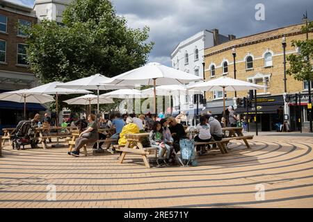 Leute, die draußen sitzen und das warme Wetter im Wimbledons Main Broadway Shopping Viertel im Südwesten Londons, England, Großbritannien genießen Stockfoto