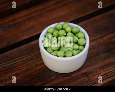 Frisch geerntete grüne Erbsen in einer Schüssel auf einem Holztisch. Schließen. Stockfoto