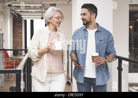 Glückliche Geschäftsleute. Mann und Erwachsene machen eine Pause mit heißen Getränken, stehen im Büro und reden. Start, Zusammenarbeit, Management Stockfoto