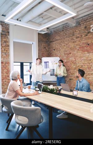 Glücklicher junger Mann und glückliche Frau, die während eines Meetings im Kreativbüro einen neuen Projektplan auf einem Whiteboard diskutieren. Start, Zusammenarbeit, Management Stockfoto