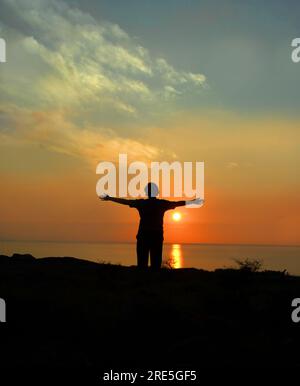 Besucher steht mit breiten Armen und verabschiedet sich von der Big Island von Hawaii. Die Sonne geht unter und endet den Tag, während ihre Reise ebenfalls endet. Stockfoto