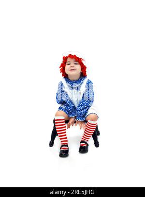 Das altmodische Puppenkostüm trägt ein süßes, kleines 3-jähriges Kind. Sie sitzt auf einem Melkhocker und grinst von Ohr zu Ohr. Stockfoto