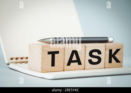 Aufgabe, Notizbuch, Stift und Holzblöcke mit dem Wort „AUFGABE“ darauf, wunderschöner hellblauer Hintergrund, Kopierraum Stockfoto