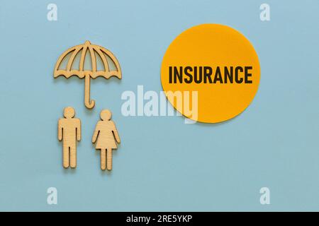 Hölzerne Figuren von Menschen unter einem Schirm, Versicherungstext auf einem wunderschönen gelben Kreis, der aussieht wie die Sonne scheint, blauer Hintergrund, Kopierraum, Stockfoto