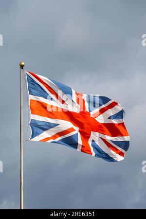 Union Jack, Flagge des Vereinigten Königreichs Großbritannien und Nordirland, fliegt im starken Wind auf einem Stab gegen bewölkten Himmel. Stockfoto