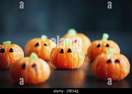 Halloween süße Kürbis-Orangenfrucht mit Schokoladenaugen. Gesunder Dessert-Snack mit lustigen Gesichtern für die Party-Dekoration des Kindes. Selektiver Fokus Stockfoto