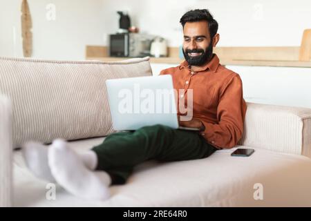 Glücklicher Inder, der als Freiberufler arbeitet und zu Hause ein Notebook benutzt Stockfoto