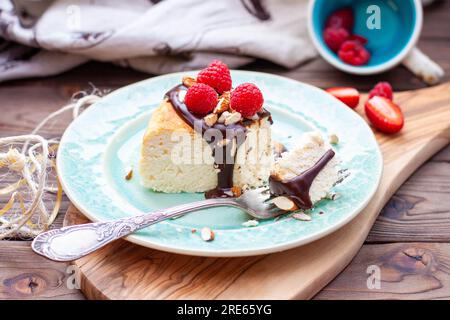 Scheibe Vanille-Käsekuchen mit Schokoladensoße, frischen Himbeeren und Nüssen auf blauem Teller, Nahaufnahme Stockfoto