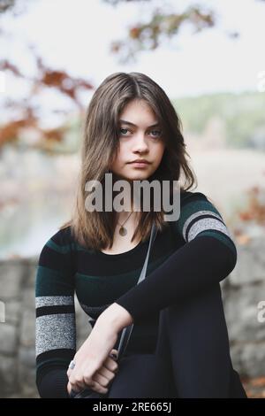 Wunderschöne braune junge Frau, die in die Kamera blickt und sich von Herbstfarben umgeben hat. Selektiver Fokus. Stockfoto