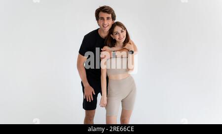 Fröhlicher junger Kaukasier, der eine Frau in Sportbekleidung umarmt, zusammen trainiert und aktiv lebt Stockfoto