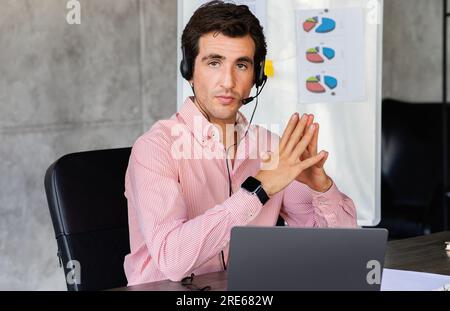 Fokussierter junger Geschäftsmann mit Kopfhörern, der Videoanrufe auf dem Laptop hält Stockfoto