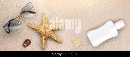 Flach liegendes Panorama am Strand, wo ein Seestern neben einer Frauensonnenbrille in goldenen Rahmen liegt. Auf dem Sand eine weiße Flasche für Sonnenöl Stockfoto