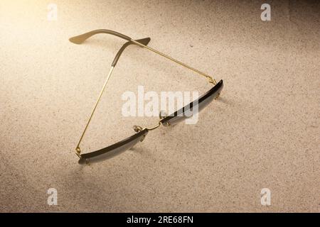 Frauen-Sonnenbrille mit goldenen Rahmen auf dem Sand in der hellen Sonne. Sommer- und Strandaccessoires. Sonnenschutz Stockfoto