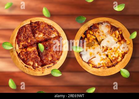 Zwei köstliche heiße indische Pizzen auf einem Holztisch. Margherita Pizza und Maispizza mit fliegenden grünen Blättern. Stockfoto